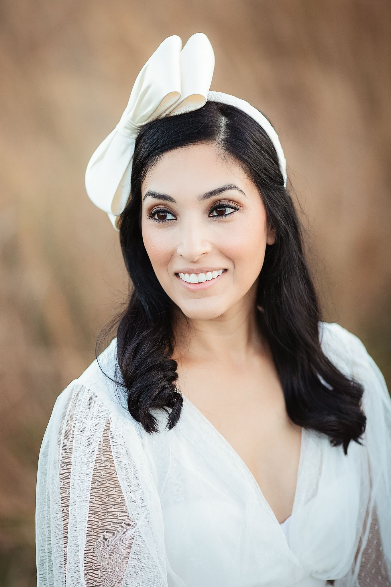 Smiling dark-haired bride wearing white satin bow headband and sheer polka dot white bridal robe.