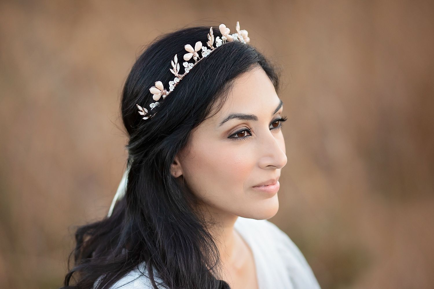 Close-up of dark-haired bride wearing gold floral leaf crown tiara against warm bokeh background.