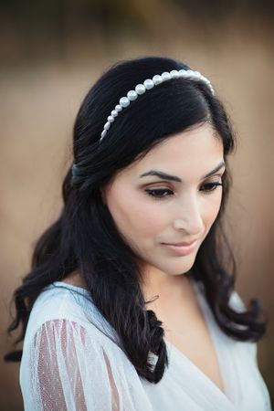Close-up portrait of dark-haired bride wearing classic pearl headband in sheer white bridal robe.