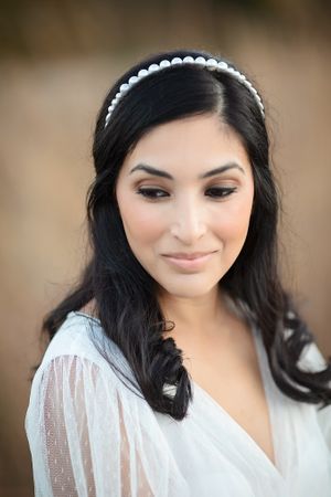 Beautiful dark-haired bride smiling softly wearing a delicate pearl headband and sheer white dress.