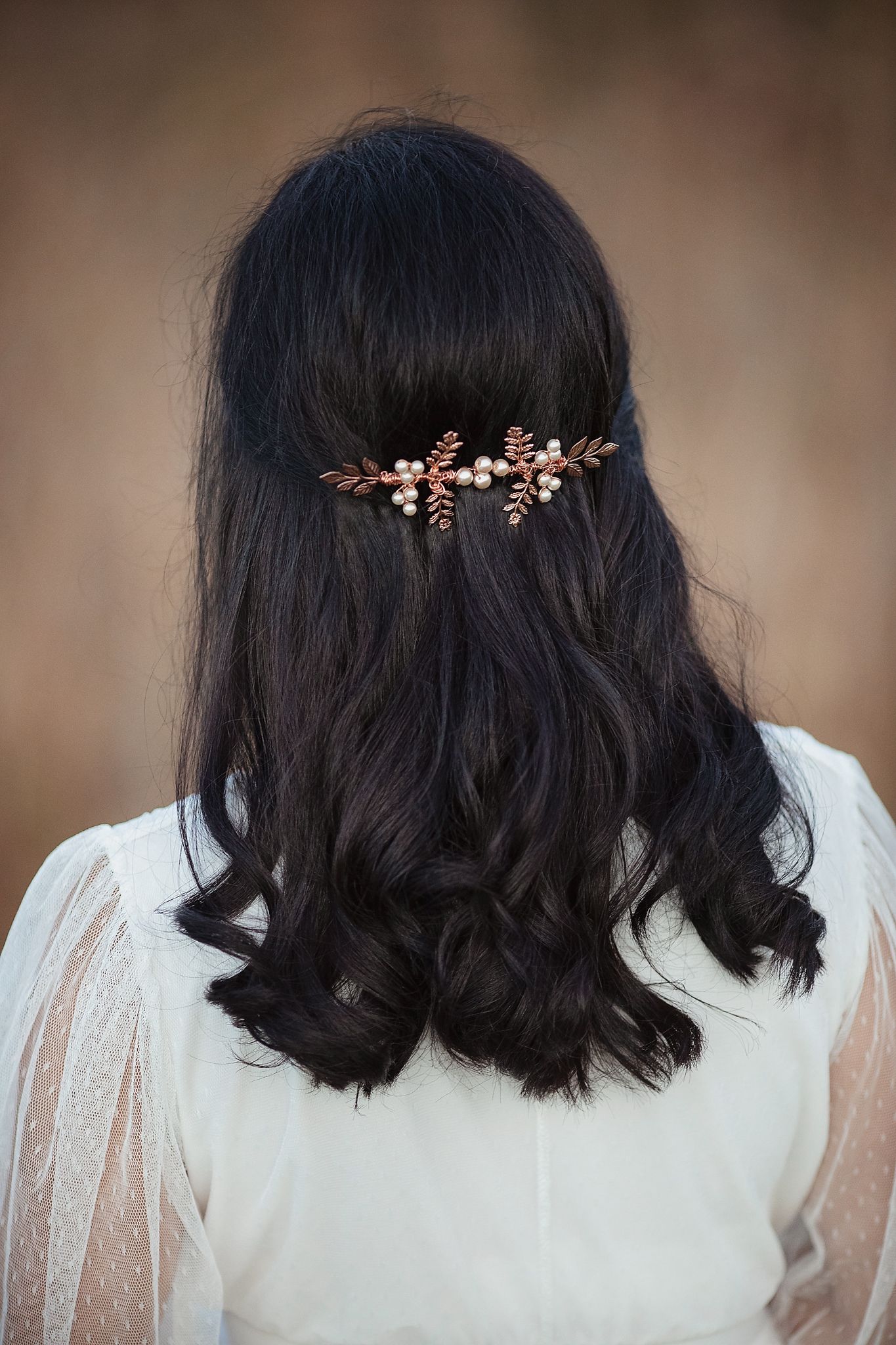 Close-up back view of dark wavy hair adorned with a delicate rose gold leaf and pearl hair comb.