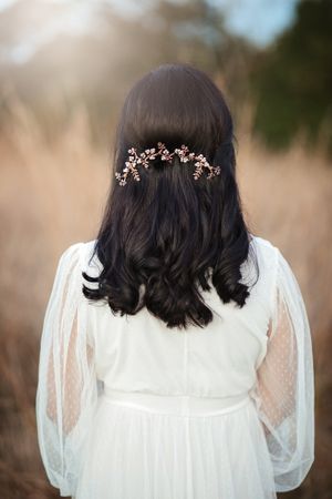 Back view of a bride with dark wavy hair styled with a rose gold floral hair vine accessory.