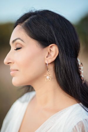 Profile of a bride with closed eyes wearing a gold star-shaped flower drop earring outdoors.