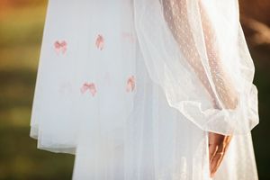Close-up of a white bridal veil with delicate pink bow appliques in a soft outdoor setting.