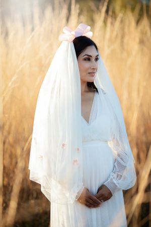 Beautiful bride wearing a white wedding dress and veil adorned with a pink bow in golden fields.