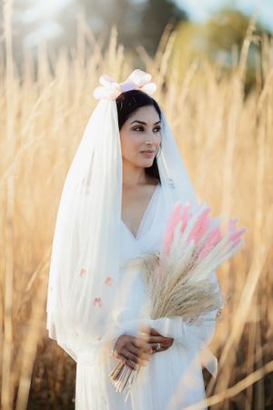 Stunning bride holding a dried floral bouquet with pink accents wearing a bow-adorned bridal veil.