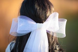 Close-up detail of a delicate white tulle bow bridal hair accessory with pearl center embellishment.