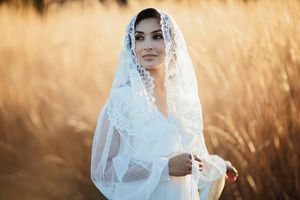 Beautiful bride wearing white lace mantilla veil in sun-kissed wheat field.