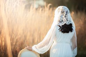 Back view of bride in white dress with lace veil in golden field.