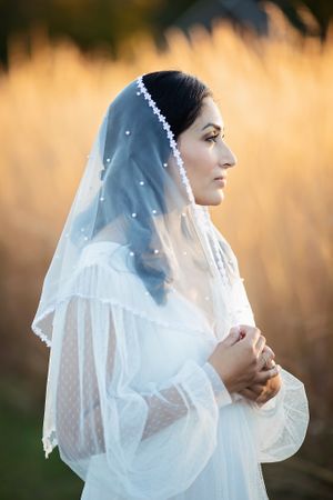 Side profile of bride in pearl-dotted veil with golden bokeh background.