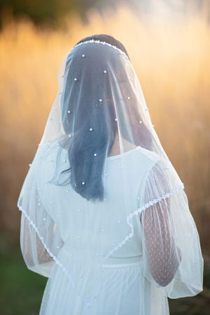 Back view of bride wearing pearl-embellished white veil and dotted white dress.