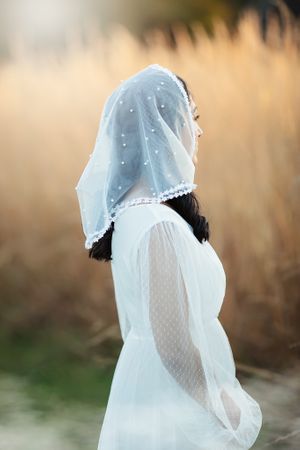 Side view of bride in white pearl chapel veil in golden wheat field.