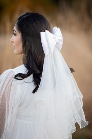 Back view of bride with white satin bow and layered veil in field.