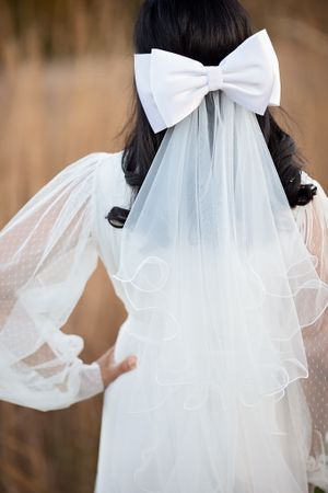 Back view of bride with large white bow and ruffled veil in wheat field.