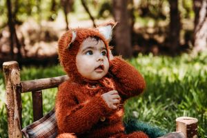 Expressive baby in fluffy brown bear costume outdoors.