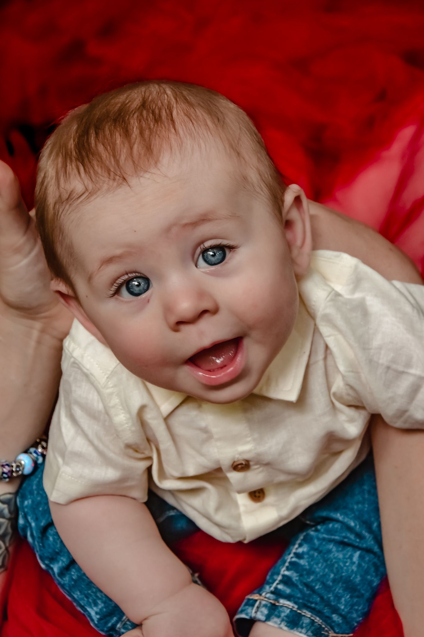 Baby in white shirt and blue pants smiling against a vibrant red background.