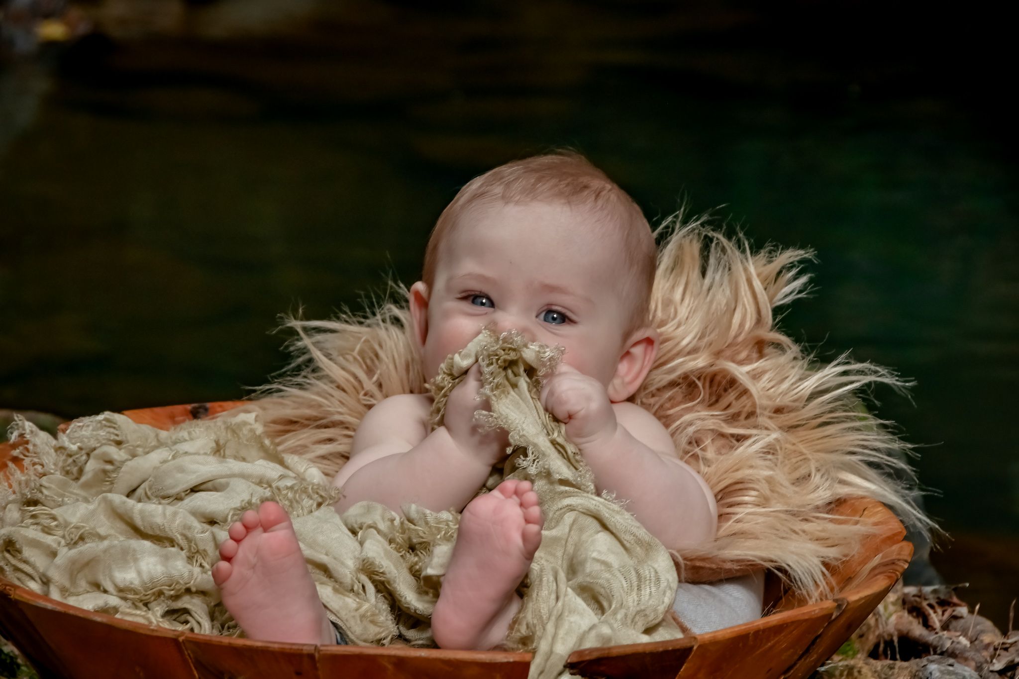 Baby lying on straw-colored material with soft natural lighting.