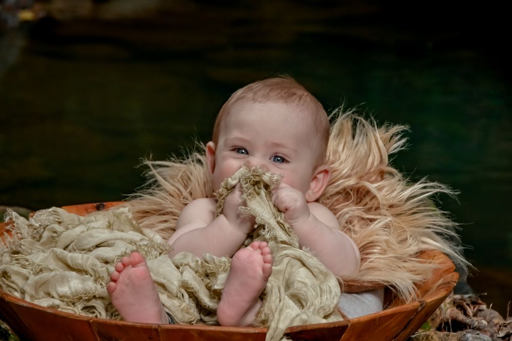 Baby lying on straw-colored material with soft natural lighting.