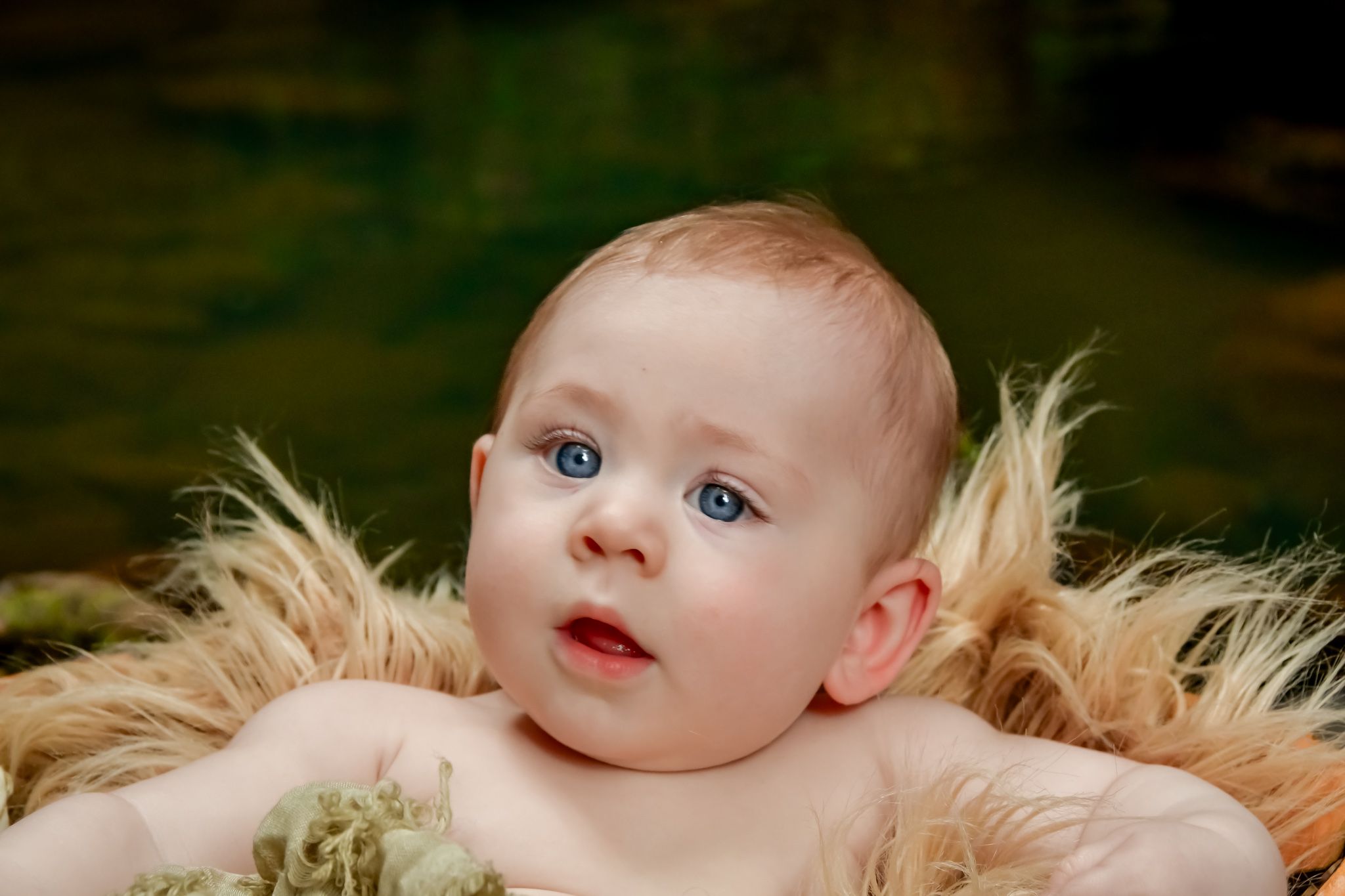 Baby portrait with bright blue eyes against dark background with soft lighting.