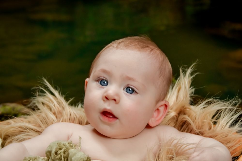 Baby portrait with bright blue eyes against dark background with soft lighting.