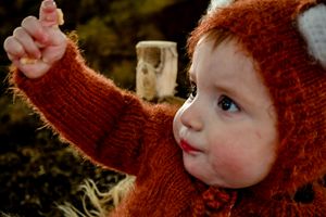 Child in red knit sweater points with wonder during outdoor autumn photoshoot.