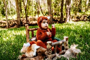 Baby wearing adorable brown bear costume lying on grass in woodland setting.