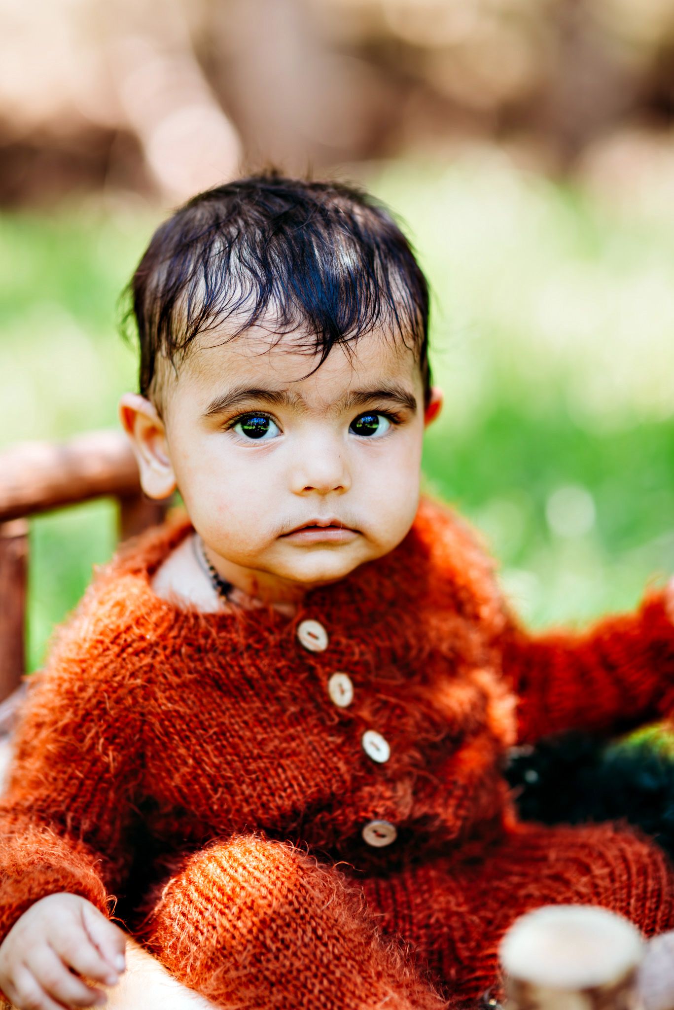 Baby wearing cozy rust-colored sweater in outdoor setting.