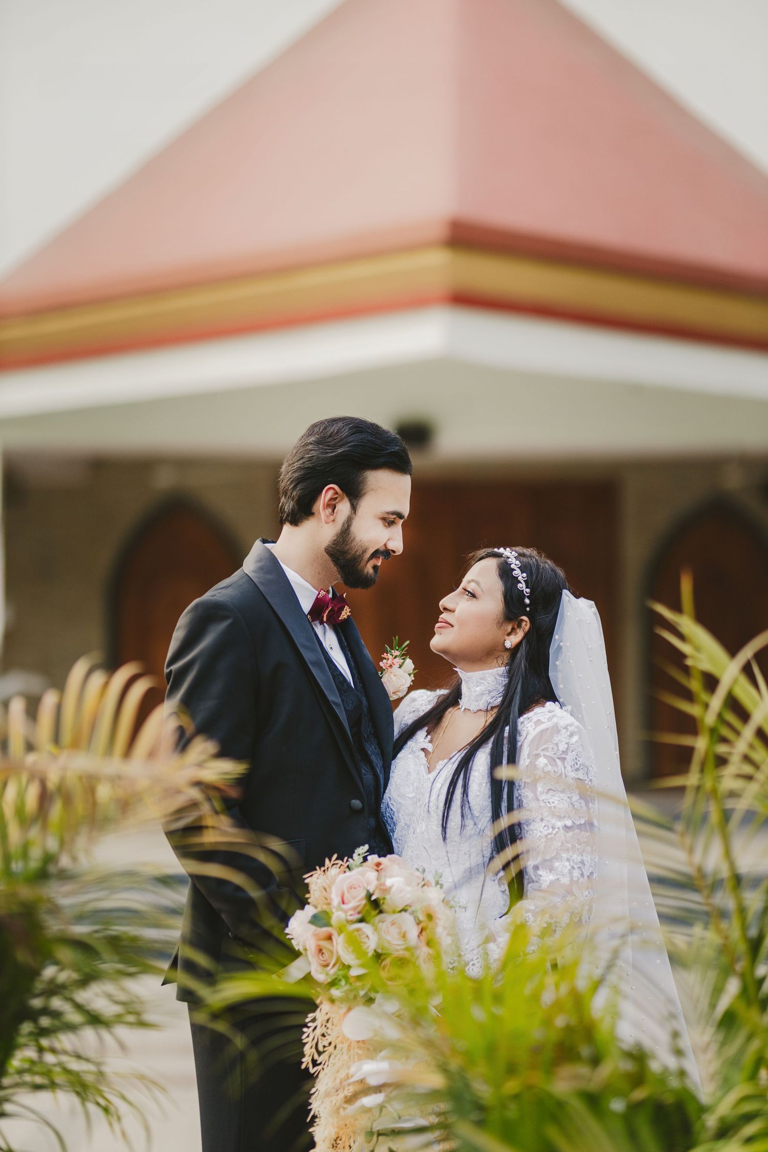 Intimate wedding portrait with couple surrounded by tropical foliage and architecture.