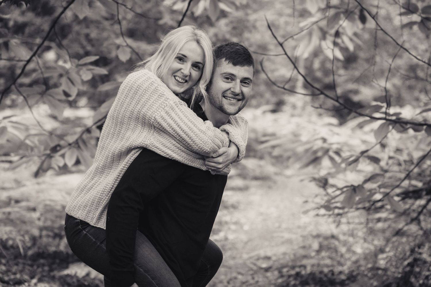 couple giving each other a piggy back in the woods
