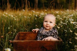 Baby sitting in wooden box surrounded by blooming wildflowers.