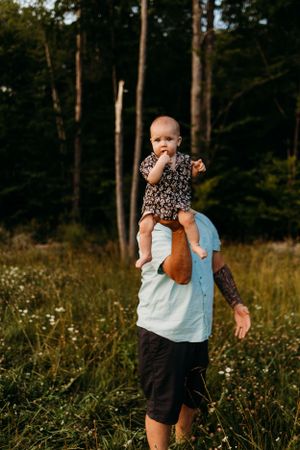 A playful outdoor family moment in a wildflower meadow at sunset with tall trees in the background.