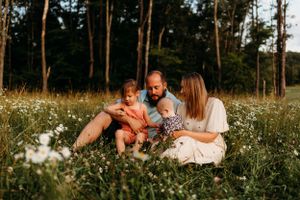 Family relaxing together in field of white daisies during sunset.