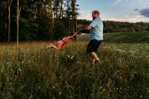 Playful swinging moment captured in a meadow with tall grass and wildflowers.