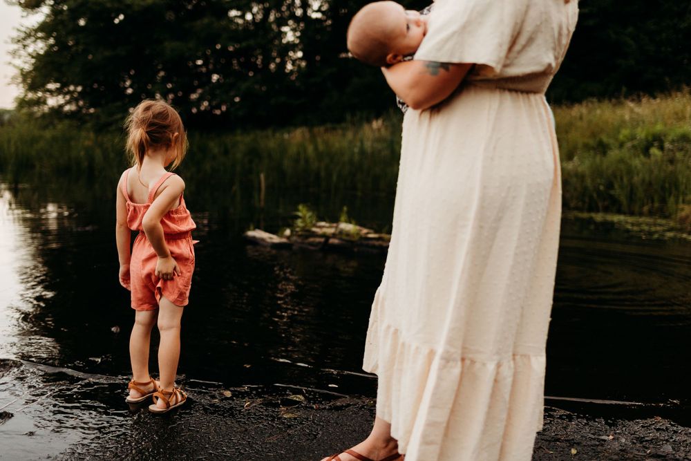 Two people standing by a serene lake edge in summer dresses during sunset.