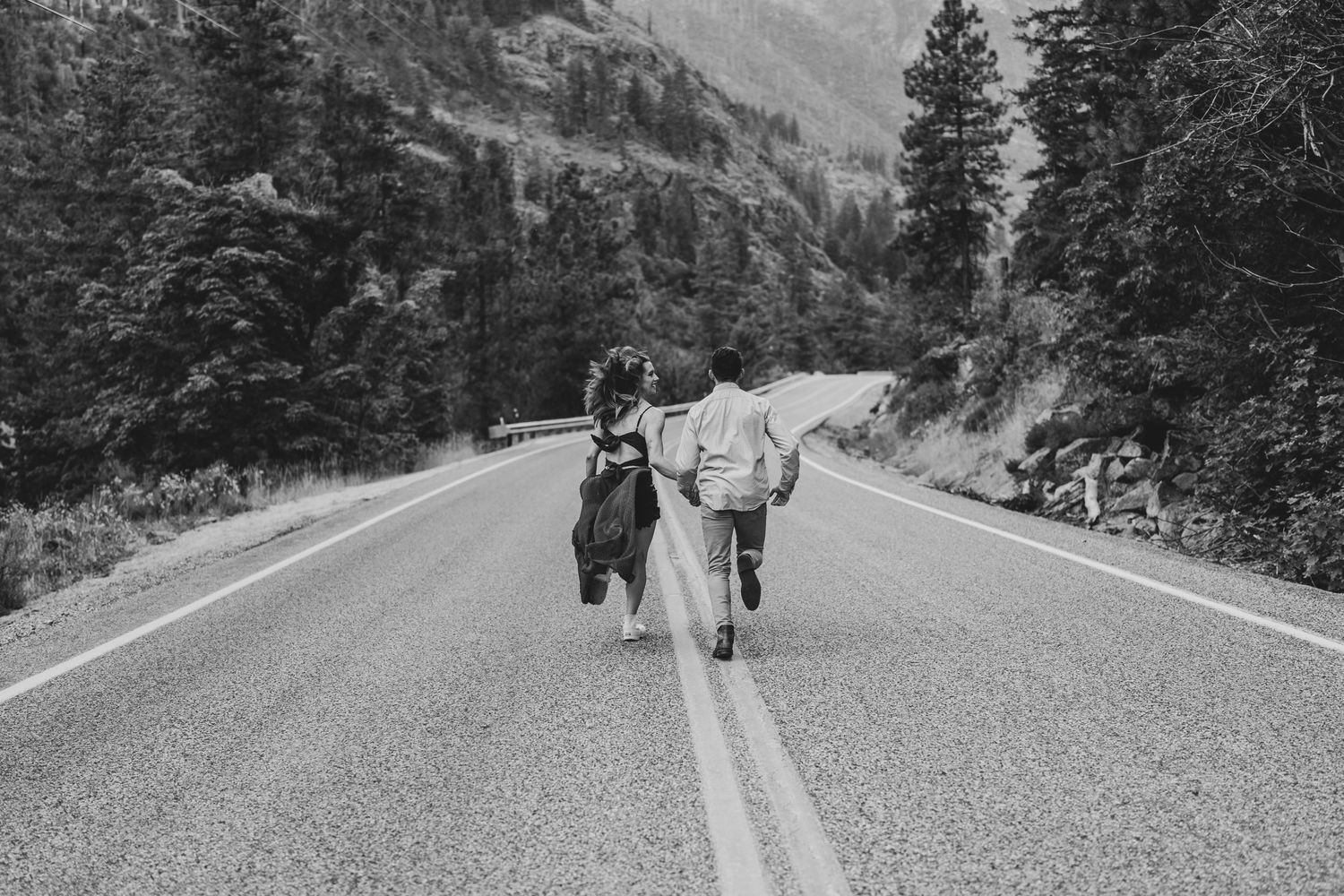 A black and white photo of a couple walking down a mountain road together.