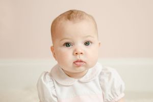 Close-up portrait of a baby with green eyes wearing a white peter pan collar outfit.