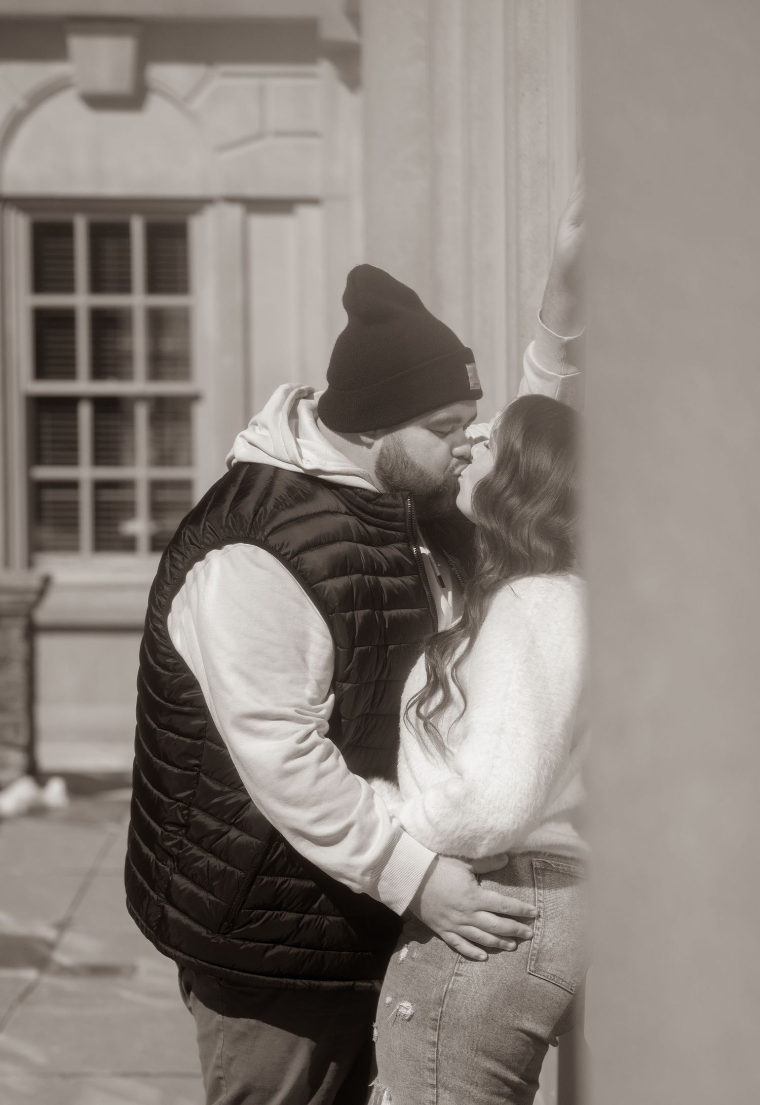 black and white image of couple leaning against a beautiful building and kissing.