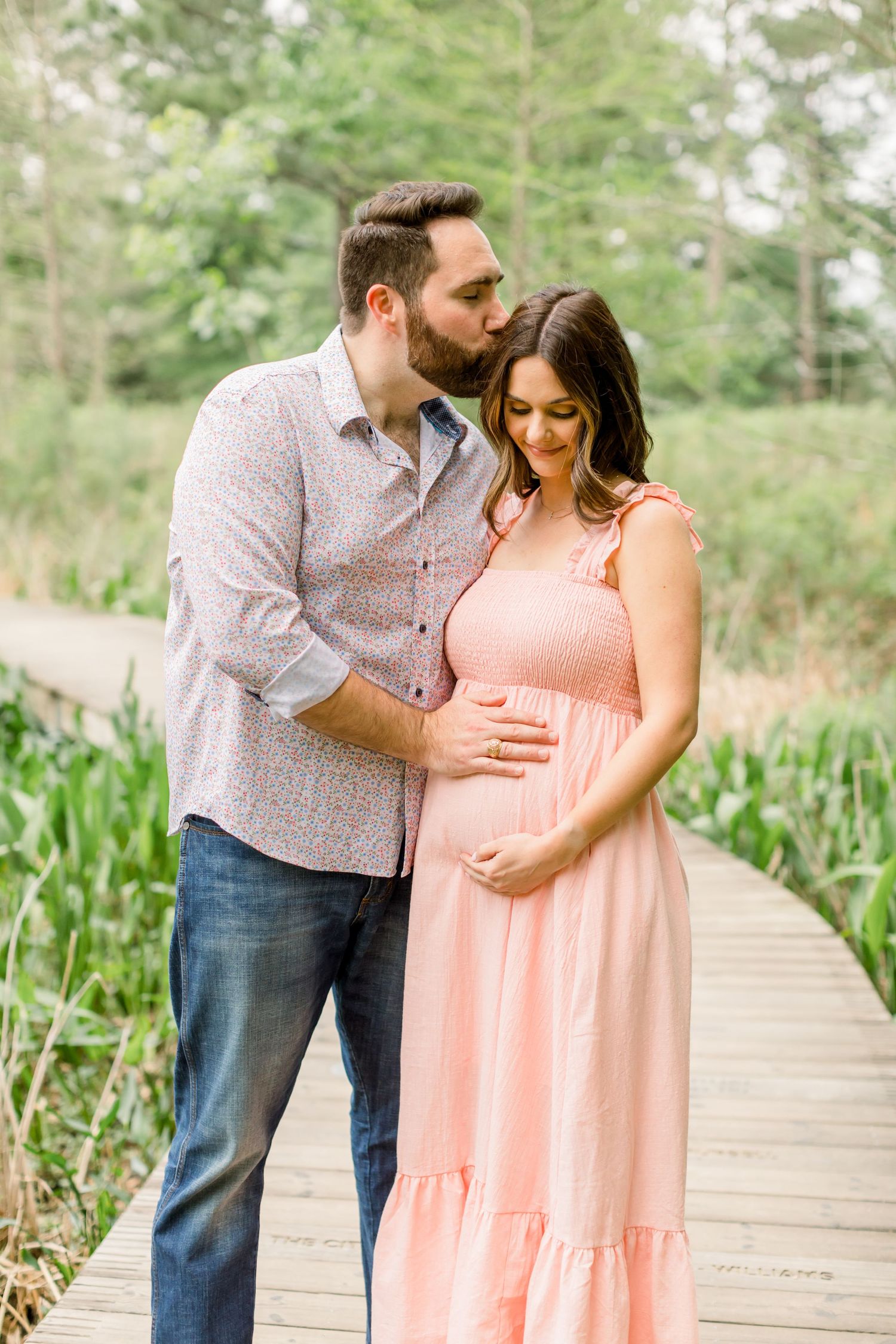 A couple shares an intimate moment on a wooden walkway during a maternity photoshoot.