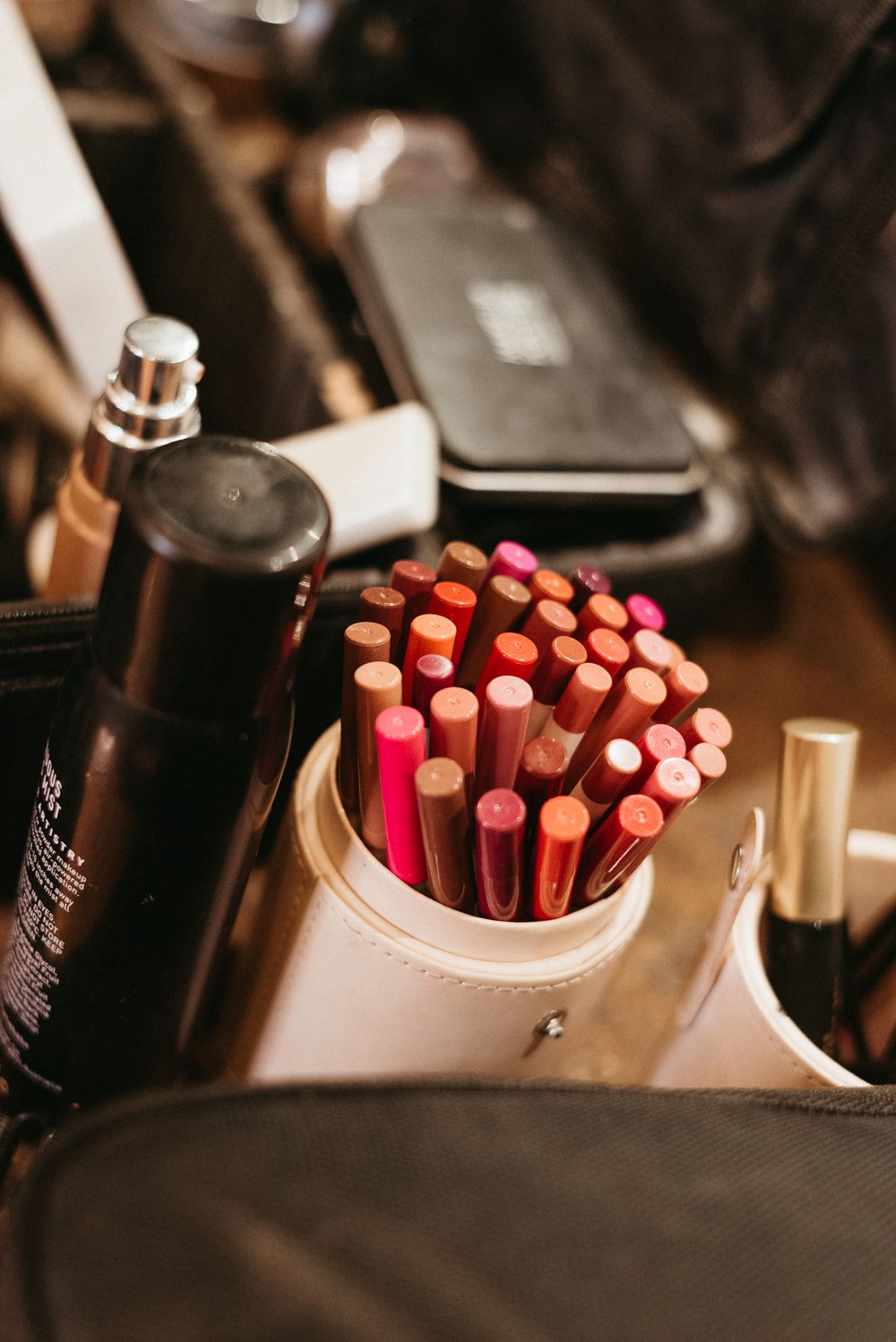 Collection of pink and red pencils arranged in a white holder alongside makeup products.
