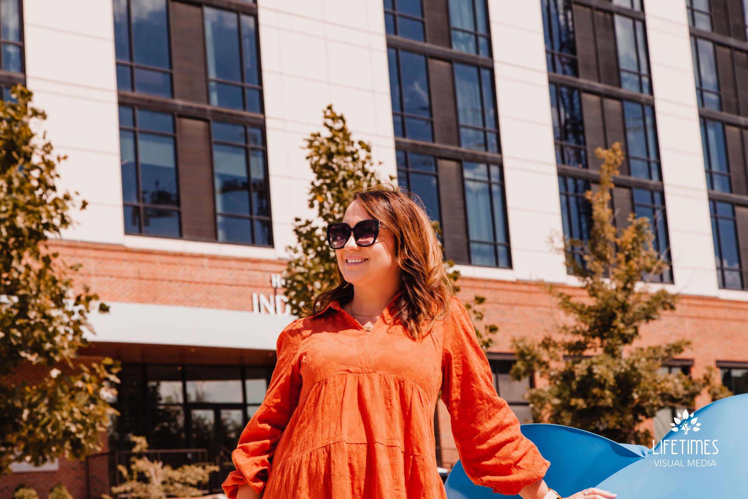 Person in bright orange dress walking past modern office building with large windows.