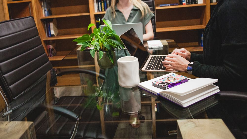Professional office meeting scene with notebooks and plants on desk in wood-paneled room.