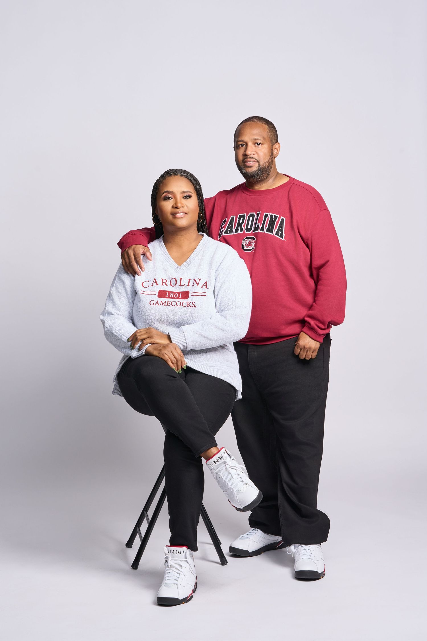 A couple wearing Carolina university sweatshirts pose together in a studio setting.