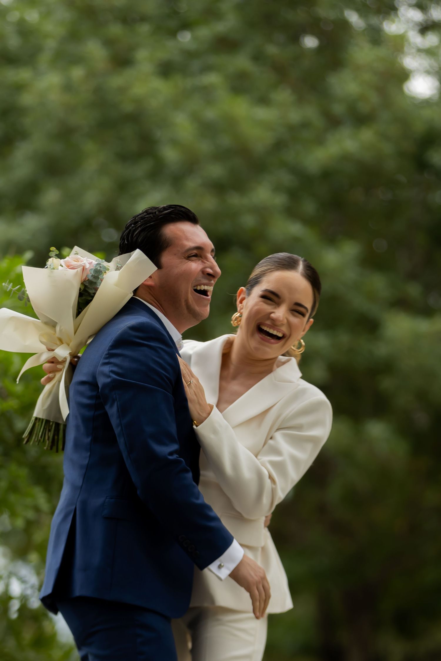 Laughing bride and groom with bouquet sharing joyful moment outdoors after wedding ceremony.