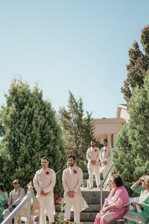 Outdoor wedding ceremony setup with guests seated on steps surrounded by evergreen trees.