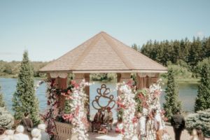 A lakeside wedding gazebo decorated with white floral arrangements and fabric draping.