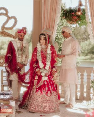 Traditional wedding ceremony with participants in red and cream attire under decorated pavilion.