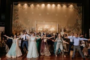 Large group of wedding guests dancing in formal attire at an elegantly decorated reception venue.