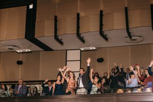 Wedding guests celebrating from a balcony with raised hands and joyful expressions.