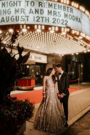 Wedding couple poses beneath illuminated theater marquee on their special night.