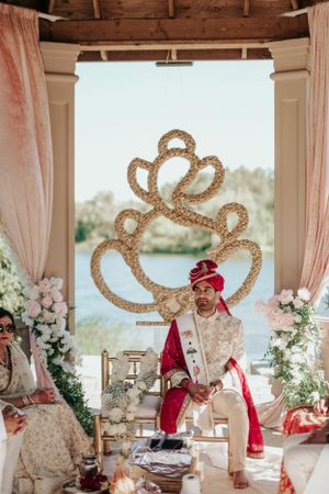 Ornate Indian wedding mandap with gold decorative elements and pink drapes overlooking a waterfront.